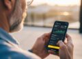 A man standing outdoors uses a cryptocurrency trading app on his smartphone. This represents mobile finance, freedom, and real-time investing.